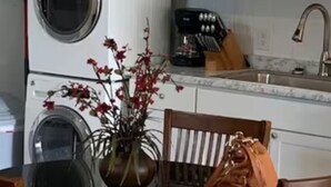A compact kitchen with white cabinets, a washing machine, and a dining area with a table and chairs. - Fully Furnished Studio Directly Across from TMH (Tallahassee)