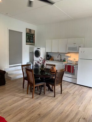A compact kitchen with white cabinets, a built-in oven, microwave, and a washing machine. There is a dining table with chairs and a vase with flowers. - Fully Furnished Studio Directly Across from TMH (Tallahassee)