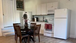 A compact kitchen with white cabinets, a white refrigerator, and a dining area with a wooden table and chairs. - Fully Furnished Studio Directly Across from TMH (Tallahassee)