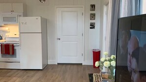 A compact kitchen with white appliances, a door, and a small table with a vase of flowers. - Fully Furnished Studio Directly Across from TMH (Tallahassee)
