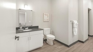 A modern bathroom with a white sink, mirror, and toilet. There is a towel rack with a white towel hanging on it. - Landing | Stylish 1BD, Rooftop Lounge, Pool (Memphis)
