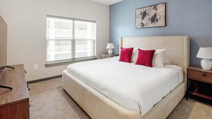 A bedroom with a large bed, two bedside tables, a window with blinds, and a piece of wall art. - Landing | Stylish 1BD, Rooftop Lounge, Pool (Memphis)