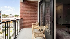 A balcony with a brick wall, two wicker chairs, and a view of the street and buildings. - Landing | Stylish 1BD, Rooftop Lounge, Pool (Memphis)