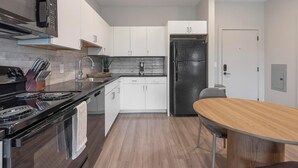 Een moderne keuken met witte kasten, een zwarte koelkast en een houten eettafel.
