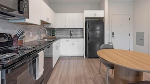 Eine moderne Küche mit weißen Schränken, einem schwarzen Kühlschrank und einem Holztisch.