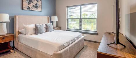 A bedroom with a bed, bedside tables, a TV, and a window with blinds.
