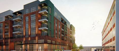 Un immeuble à plusieurs étages dont la façade est un mélange de briques et de verre, doté de balcons et d’une cour intérieure aménagée avec des espaces pour s’asseoir et de la verdure.