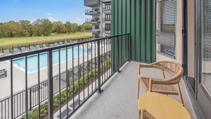 Een balkon met uitzicht op een zwembad, een rieten stoel en een groene wand.