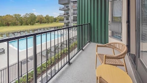 Ein Balkon mit Blick auf einen Swimmingpool, einem Korbstuhl und einer grünen Wand.