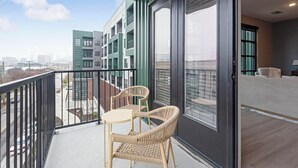 A balcony with wicker chairs and a table, overlooking a cityscape with modern buildings. - Landing | Amazing 1BD, Rooftop Lounge, Yoga Studio (Memphis)