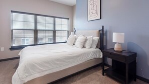 A bedroom with a bed, a nightstand, a lamp, and a window with blinds. - Landing | Stunning 1BD, Rooftop Lounge, Gym (Memphis)