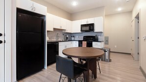 A compact kitchen with white cabinets, a black refrigerator, a microwave, and a dining area with a round table and two chairs. - Landing | Amazing 1BD, Rooftop Lounge, Yoga Studio (Memphis)