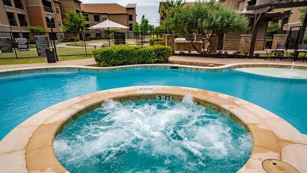 A hot tub with a 4 FT and 3 FT depth marking, surrounded by a pool and a fenced patio area with lounge chairs and a pergola. - Landing | Spectacular 1BD, Clubhouse, Pool (Grand Prairie)