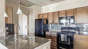 A modern kitchen with granite countertops, stainless steel appliances, and wooden cabinets. - Landing | Spectacular 1BD, Clubhouse, Pool (Grand Prairie)