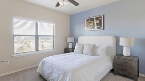 A bedroom with a bed, two bedside tables with lamps, a ceiling fan, a window with blinds, and a wall-mounted painting. - Landing | Stylish 1BD, Clubhouse, Gym (Grand Prairie)