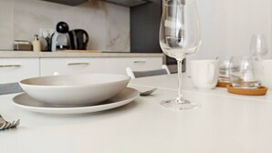 Une cuisine moderne avec des meubles blancs, un pare-feu en marbre et un coin repas agrémenté d’une table blanche, de l’assiette, d’un verre et d’une tasse.