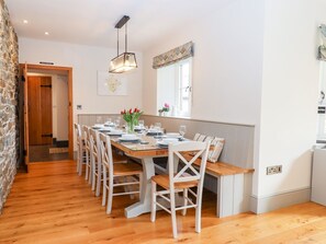 A dining area with a long wooden table set for six, white chairs, and a hanging light fixture.