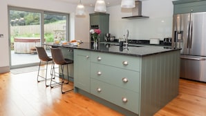 A modern kitchen with a large island, stainless steel appliances, and pendant lighting. - Knowle House (Okehampton)