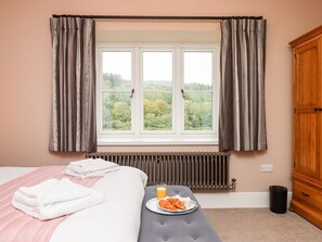 A bedroom with a bed, a bedside table with a plate of croissants and orange juice, a radiator, and a window with curtains.