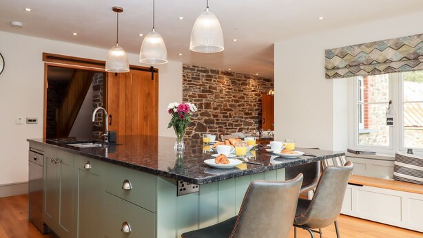 A modern kitchen with a large island, pendant lights, and a stone accent wall. - Knowle House (Okehampton)