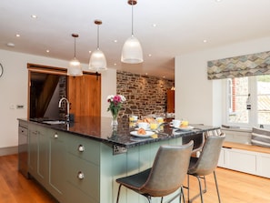 A modern kitchen with a large island, pendant lights, and a stone accent wall. - Knowle House (Okehampton)