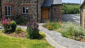 A stone house with a wooden door, a brick window, and a garden with various flowers. - Knowle House (Okehampton)
