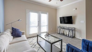A living room with a sofa, coffee table, and TV stand. - Landing | Spectacular 2BD, Clubhouse, Pool (Grand Prairie)