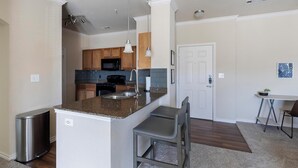 A compact kitchen with granite countertops, a stainless steel sink, and wooden cabinets. - Landing | Spectacular 2BD, Clubhouse, Pool (Grand Prairie)