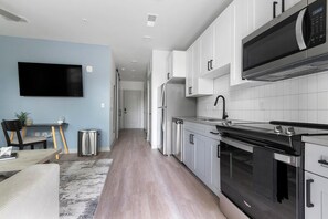 A modern kitchen with white cabinets, a black stove, and a microwave. - Landing | Beautiful Studio, Game Room, Gym (Jacksonville)
