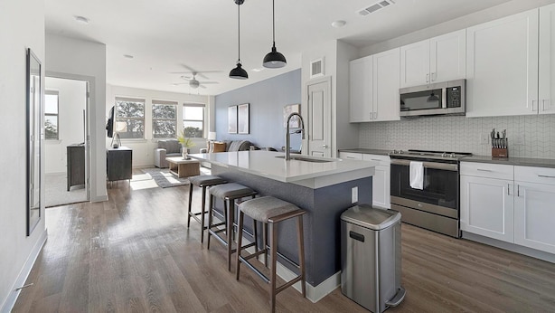 A modern kitchen with a central island, bar stools, stainless steel appliances, and a view of the living area. - Landing | Incredible 1BD, Gym, Clubhouse (Austin)