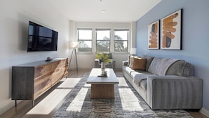 A modern living room with a flat-screen TV, a wooden cabinet, a grey sofa, and a coffee table. - Landing | Incredible 1BD, Gym, Clubhouse (Austin)