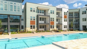 A modern apartment complex with a swimming pool, multiple balconies, and a mix of light and dark siding. - Landing | Incredible 1BD, Gym, Clubhouse (Austin)