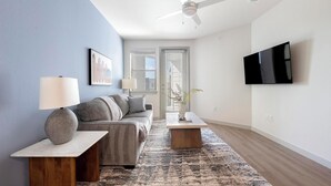 En moderne stue med sofa, to sofaborde, et sofabord, et fjernsyn monteret på væggen og en loftventilator.
