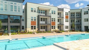 Un moderno complejo de apartamentos con piscina, varios balcones y una combinación de revestimiento claro y oscuro.