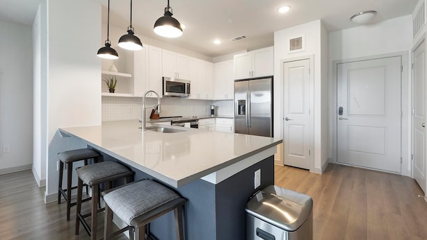 Una cocina moderna con armarios blancos, una isla grande con taburetes de bar, electrodomésticos de acero inoxidable e iluminación colgante.