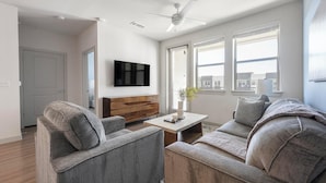 Una sala moderna con un sofá gris, dos sillones, una mesa de centro de madera y un televisor de pantalla plana montado en la pared.