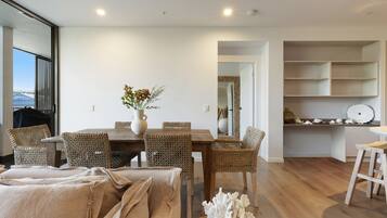 A dining area with a wooden table and woven chairs, a vase with flowers, and a view of the outdoors through a window.