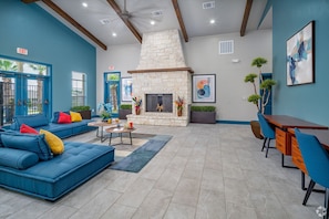 A spacious living area with a stone fireplace, blue sofas, a dining table, and a view of the outside. - Landing | Amazing 2BD, Gym, Clubhouse (San Antonio)