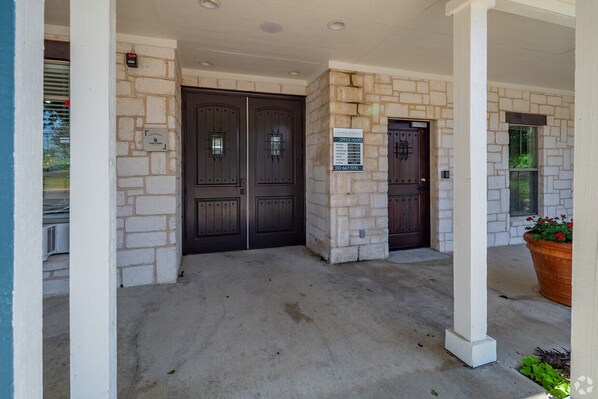 A building entrance with two dark wooden doors, a stone wall, and a concrete floor. - Landing | Amazing 2BD, Gym, Clubhouse (San Antonio)