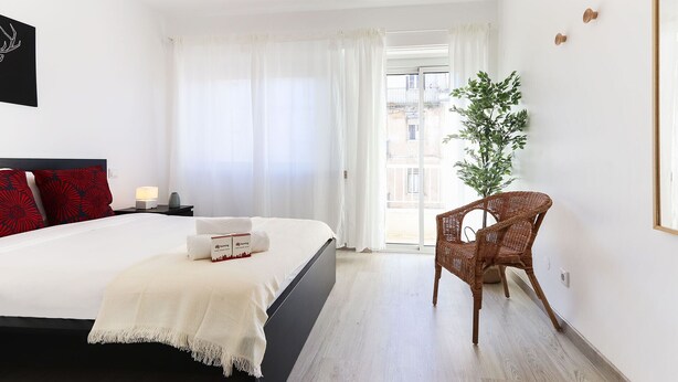 A hotel room with a bed, a chair, a plant, and a window with curtains. - Nine Horizons Central (Lisbon)