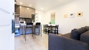 A modern kitchen with a microwave, stove, and sink, a dining area with a table and chairs, and a gray sofa in a living area. - Nine Horizons Central (Lisbon)