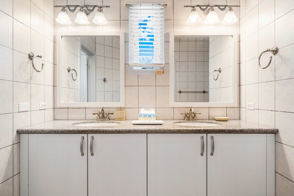 A bathroom with two sinks, a mirror, and a window with blinds.