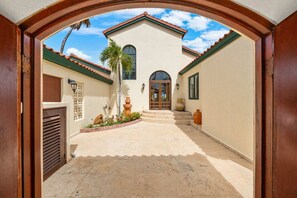 A building with a tiled roof, a central entrance with steps, and a palm tree. - Private pool • BBQ • Ocean views (Noord)