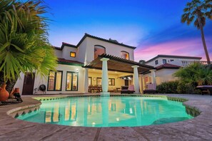 A pool with a patio area, a covered seating space, and a building with a tiled roof. - Private pool • BBQ • Ocean views (Noord)