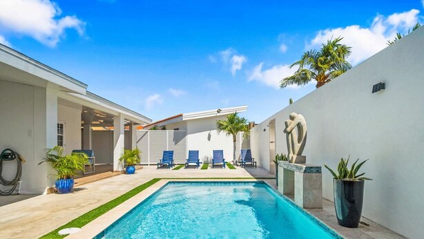 A swimming pool with a clear blue water, surrounded by a white wall and a small garden area with potted plants. - Private pool • 5 min drive to beach • BBQ (Noord)