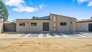 A modern two-story house with a flat roof, a front entrance with a door, and a driveway leading to the garage. - Private pool • 5 min drive to beach • BBQ (Noord)