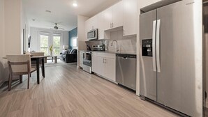 Une cuisine moderne dotée d’appareils électroménagers en acier inoxydable, un coin repas avec une table et des chaises en bois, et une vue sur l’extérieur grâce à de grandes fenêtres.
