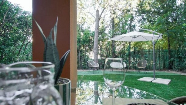 Una mesa de vidrio con sillas y un paraguas blanco en un jardín.