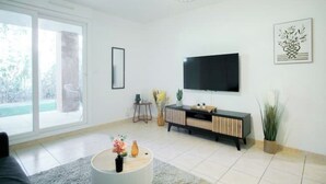 Un moderno salón con un televisor de pantalla plana grande, una mesa de centro redonda con objetos decorativos, un aparador negro y un ventanal corredero que da a un área exterior.