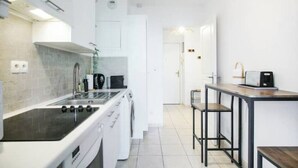 Una cocina moderna con estufa, lavamanos y lavadora, un pequeño comedor con taburetes, y una puerta que da a otra habitación.